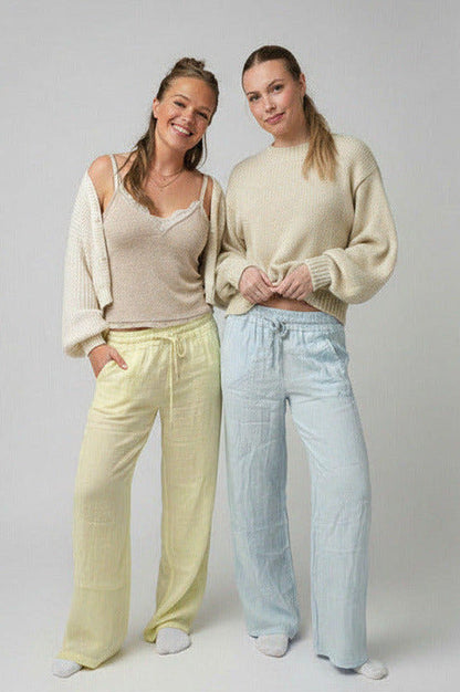 Two women standing side by side wearing light-colored outfits against a plain background