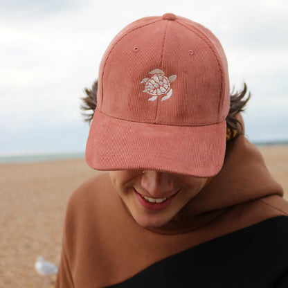 Person wearing a pink cap with a turtle design on a beach