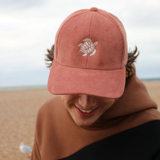 Person wearing a pink cap with a turtle design on a beach